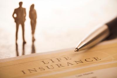 couple walking on beach in background with life insurance policy in focus in foreground
